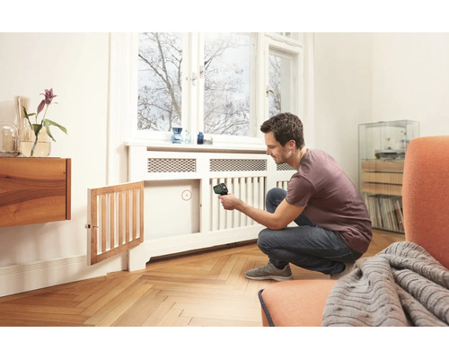 Ein Mann verwendet ein Thermometer zur Messung der Temperatur eines Heizkörpers in einem hellen Raum.