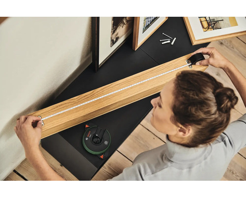 Frau misst mit einem Rollmeter einen Bilderrahmen auf einem Möbelstück