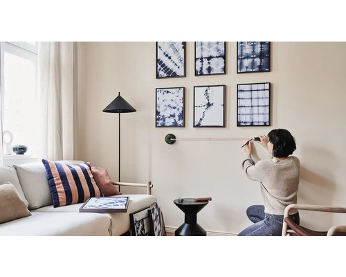 Wohnzimmer mit an der Wand hängenden Bildern, eine Person richtet die Bilder mit einem Laser aus