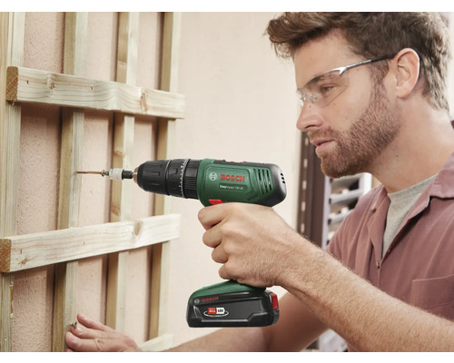 Mann schraubt Schraube mit Akkuschrauber in Holzkonstruktion