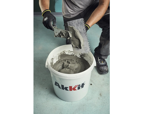 Handwerker entnimmt Fliesenkleber mit einer Kelle aus einem Eimer von Akkit