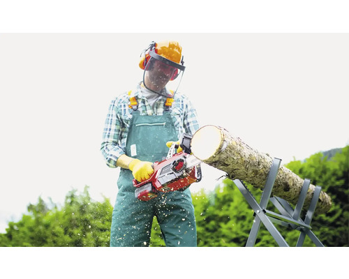 Mann mit Schutzhelm sägt mit einer Kettensäge Holz auf einem Sägebock.