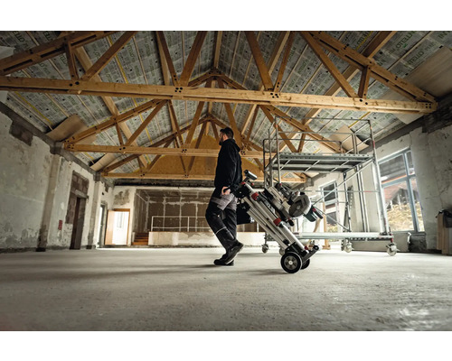 Mann transportiert ein Gerüst auf Rollen in einem Raum mit Holzbalken.