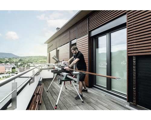 Mann schneidet Holzleiste mit einer Kappsäge auf einem Balkon.
