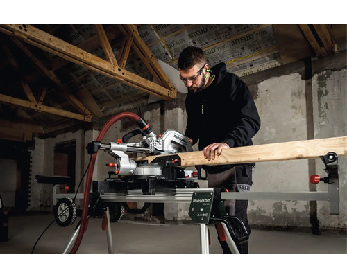 Mann sägt Holz mit einer Metabo Kappsäge auf einem Kappsägeständer in einem Rohbau.