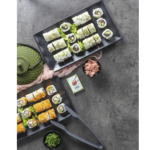 Zwei Servierplatten mit Sushi, Ingwer, Algen, Teekanne und Sushi-Zange auf einem Tisch