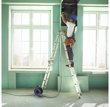 Handwerker auf einer Leiter befestigt Schallschutzplatten an einer Wand in einem Raum.