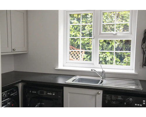 Heller Waschraum mit Spüle, Fenster und Waschmaschine.