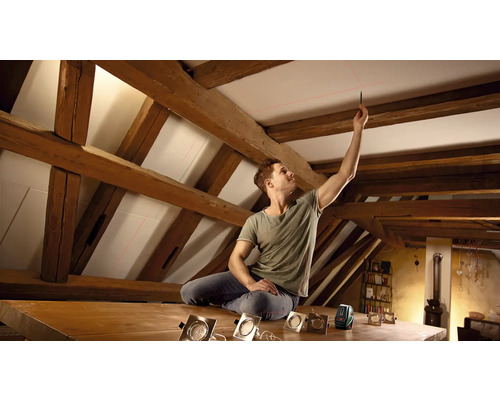 Mann mit Laser-Wasserwaage beim Ausrichten von Deckenspots unter Holzbalken