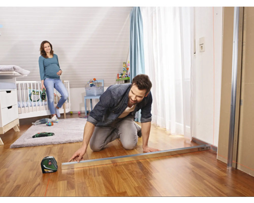 Ein Mann arbeitet mit einem Laser-Nivelliergerät in einem Kinderzimmer, während eine schwangere Frau im Hintergrund steht.