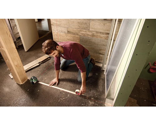 Mann arbeitet mit einem Linienlaser auf dem Boden, um eine Linie zu markieren.