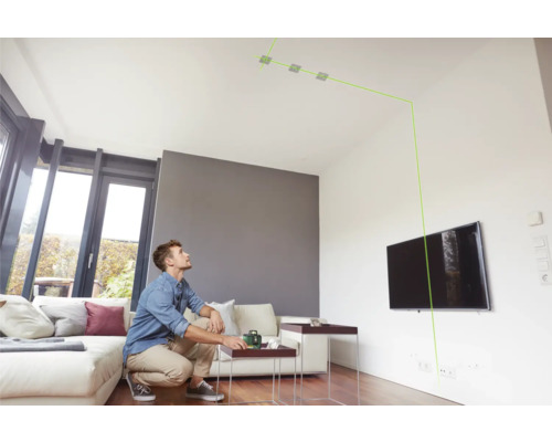 Mann benutzt Laser-Wasserwaage in einem Wohnzimmer zur Ausrichtung