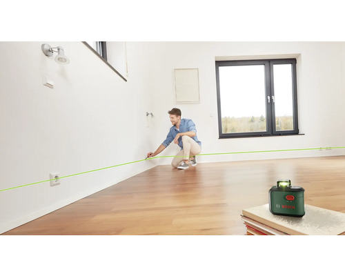 Ein Mann benutzt einen Linienlaser von Bosch, um eine grüne Linie an einer Wand in einem Raum zu markieren.