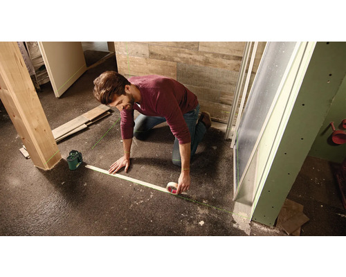 Mann markiert mit Linienlaser und Klebeband eine Bodenfläche