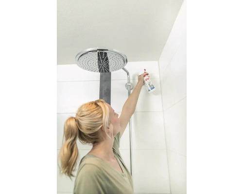 Frau reinigt Duschkopf mit Reinigungsspray im Badezimmer.