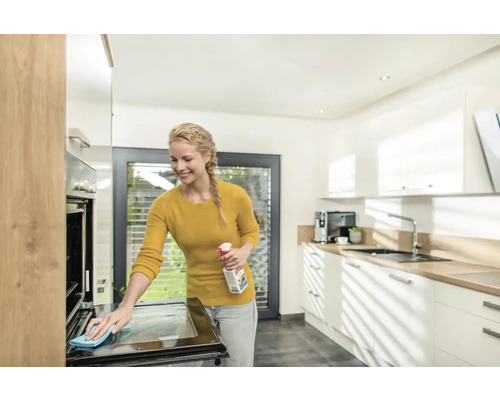 Frau reinigt mit Reiniger und Tuch einen Backofen in einer Küche