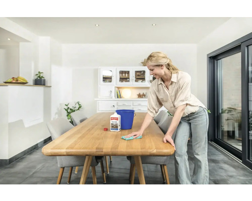 Frau reinigt Holztisch mit Reiniger und Tuch in hellem Esszimmer.