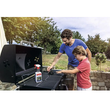 Vater und Sohn reinigen einen Grill mit Grillreiniger und Bürste im Freien.