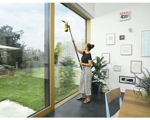 Frau reinigt Fenster mit einem Fenstersauger im Innenraum.