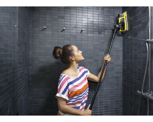 Frau reinigt eine geflieste Dusche mit einem Fensterabzieher mit Teleskopstiel