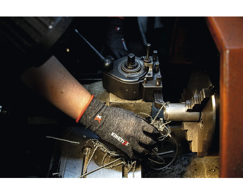 Eine Person trägt Arbeitshandschuhe an einer Drehmaschine mit Metallspänen.