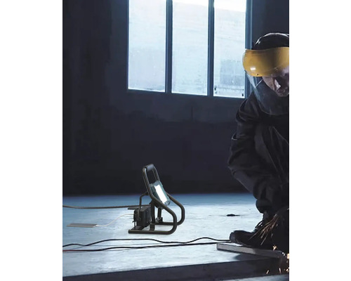 Arbeiter bei der Metallbearbeitung mit einem Baustrahler zur Ausleuchtung des Arbeitsbereichs.