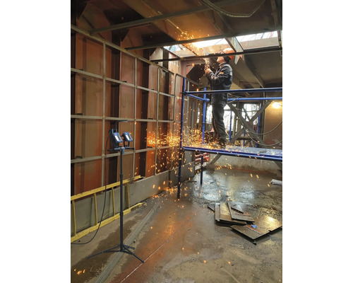 Ein Arbeiter steht auf einem Gerüst und schneidet Metall mit einer Schneidemaschine, wobei Funken fliegen.