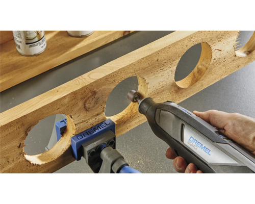 Dremel Multifunktionswerkzeug beim Bearbeiten eines Holzstücks mit runden Aussparungen, befestigt mit einer Schraubzwinge