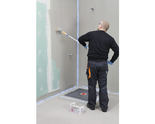 Handwerker beschichtet eine Badezimmerwand mit einer Farbrolle. Vorbereitetes Badezimmer mit Abdichtung und Duschablauf.