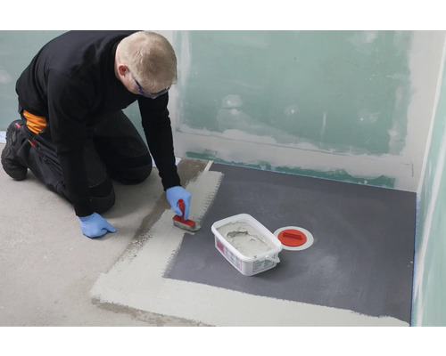 Mann dichtet Badezimmerboden mit Dichtmasse ab