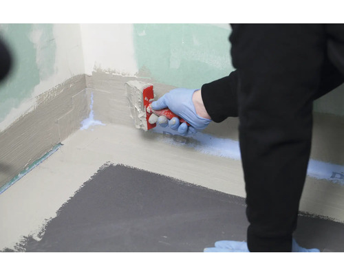 Eine Person dichtet mit einer Glättkelle eine Badezimmerecke ab.