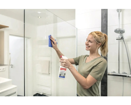 Frau reinigt Duschkabine mit Glasreiniger und Tuch im Badezimmer.