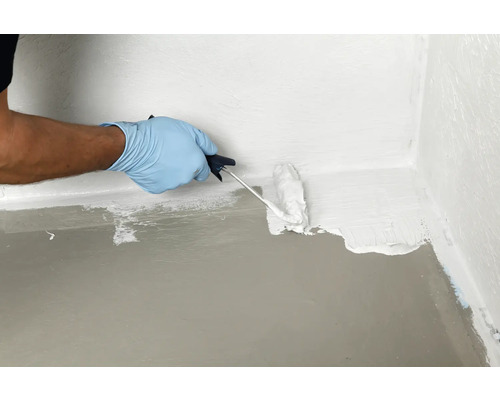 Eine Person versiegelt eine Bodenwand Ecke mit einer Farbwalze und einer wasserdichten Beschichtung.