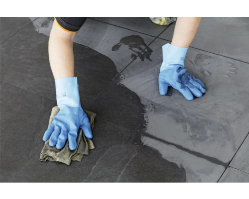 Eine Person wischt mit einem Tuch und Handschuhen Fliesen.