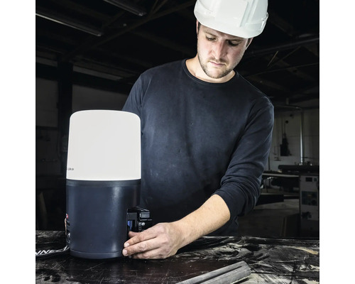 Ein Mann mit Schutzhelm montiert eine LED-Baustellenleuchte.