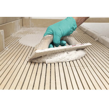 Fliesenleger mit Zahnspachtel und Fliesenkleber bei der Arbeit