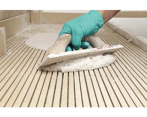 Fliesenleger mit Zahnspachtel und Fliesenkleber bei der Arbeit