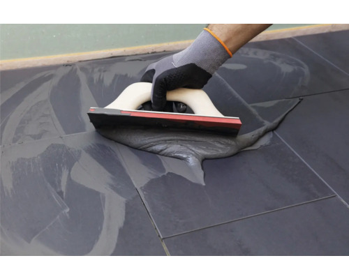 Eine Person verwendet eine Spachtelmasse zum Verfugen von Fliesen.