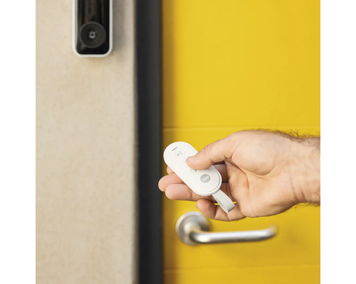 Hand mit Yale Fernbedienung vor einer Haustür mit Videokamera