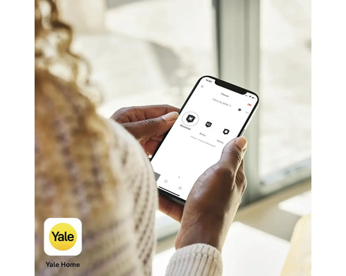 Eine Person hält ein Smartphone mit der Yale Home App zur Steuerung eines Alarmsystems.