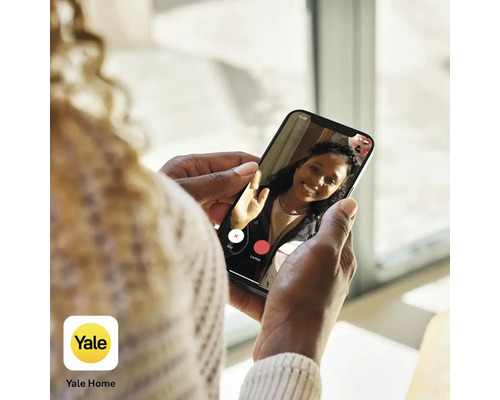 Eine Person hält ein Smartphone mit der Yale Home App in der Hand und führt einen Videoanruf.