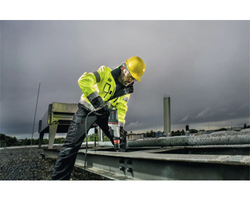 Ein Mann mit Schutzhelm und Sicherheitsweste bohrt mit einer Bohrmaschine in Metall.
