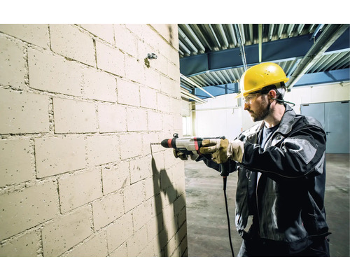Ein Handwerker bohrt mit einer Bohrmaschine ein Loch in eine Ziegelwand.