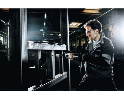 Ein Mann bohrt mit einer Bohrmaschine ein Metallgestell, wobei er eine Schutzbrille trägt.