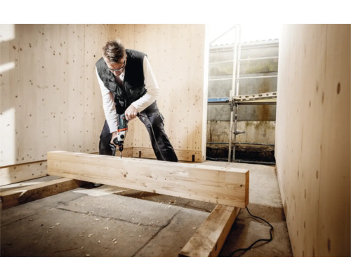 Ein Mann bohrt mit einer Bohrmaschine in einem mit Holz verkleideten Raum.