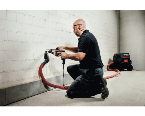 Handwerker bohrt mit Bohrhammer ein Loch in eine Wand, Staubabsaugung angeschlossen