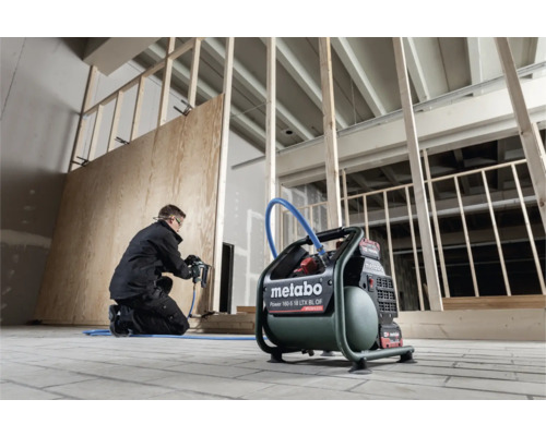 Handwerker befestigt mit einem Druckluftnagler eine Holzplatte an einer Wand, mit einem Metabo Kompressor im Vordergrund