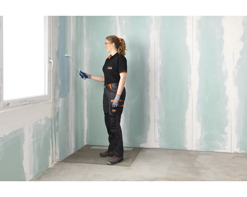 Frau streicht Wand in einem Zimmer mit einer Farbwalze.
