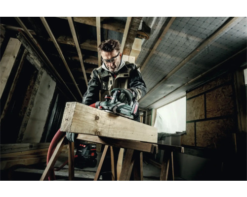 Handwerker hobelt Holzbalken mit einem Elektrohobel der Marke Metabo in einem Dachgeschoss.