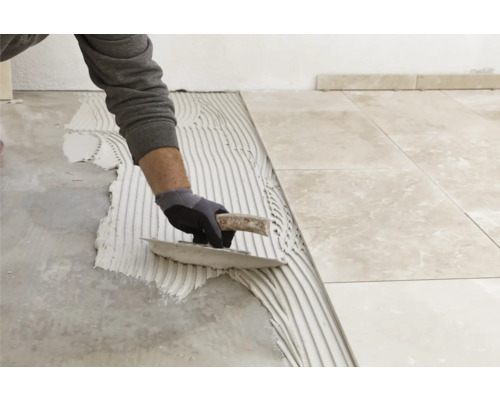 Fliesenleger trägt Kleber auf Boden auf